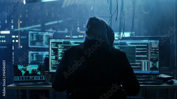 Fototapeta Dangerous Hooded Hacker Breaks into Government Data Servers and Infects Their System with a  Virus. His Hideout Place has Dark Atmosphere, Multiple Displays, Cables Everywhere.