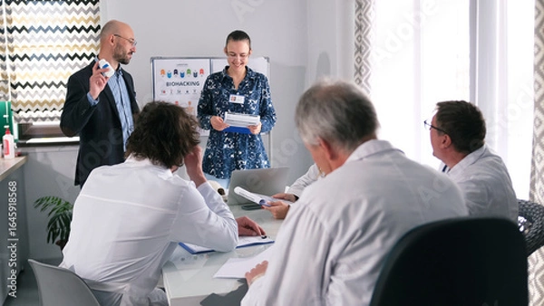 Fototapeta A happy man and a woman present to a group of doctors a new development by scientists - flu pills. A group of doctors attentively listens to the presentation