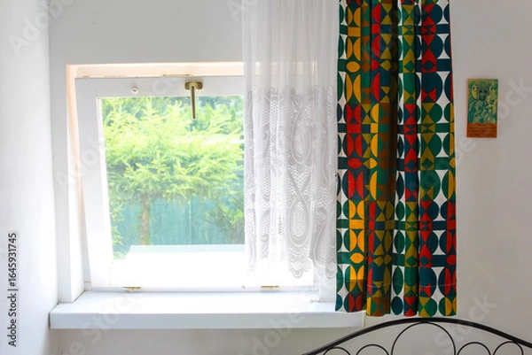 Fototapeta Modern bedroom window with colorful geometric patterned curtains and view of lush green garden landscape