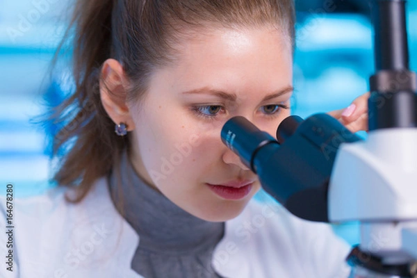Fototapeta Young woman scientist looking a microscope in a laboratory. Girl scientist doing microbiological research