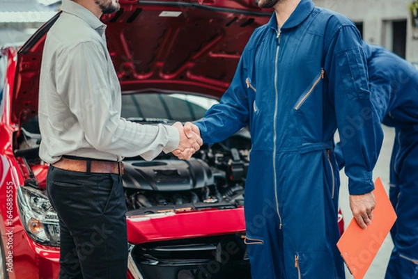 Fototapeta Car owner shaking hands with professional mechanic in clean workshop, symbolizing successful repair, trust, and complete customer satisfaction in automotive service industry.