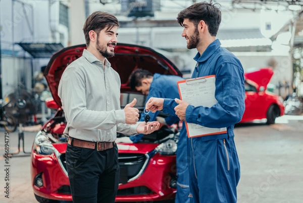 Fototapeta Smiling car owner receiving keys from mechanic after repair, symbolizing quality service, trust, and customer satisfaction in automotive maintenance.