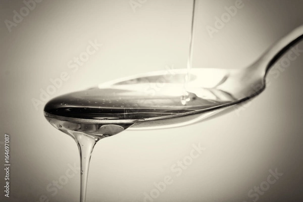 Obraz Honey pouring from spoon against a light background
