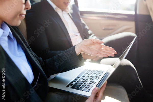 Obraz Serious man and woman discussing in a car with laptop