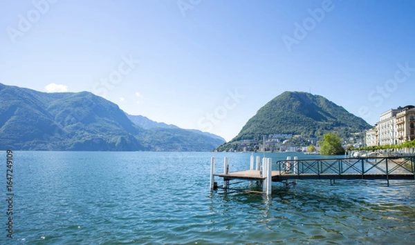 Fototapeta Detail of an old pier on Lake Ceresio in Lugano.
A sunny day and extraordinary landscape with a view of Mount San Salvatore. No people.