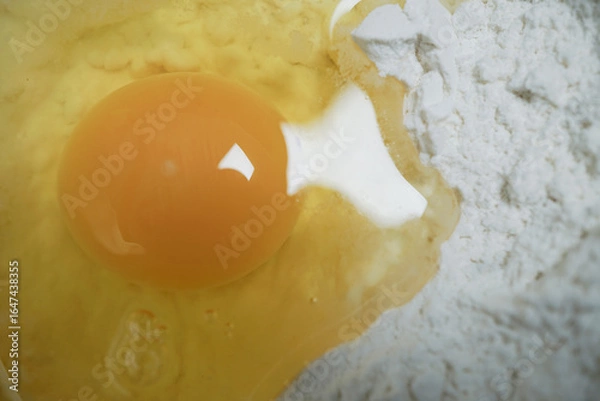 Fototapeta Close up of raw egg with bright yellow yolk sits next to pile of white flour, ready for baking. image captures smooth texture of yolk and powdery surface of flour