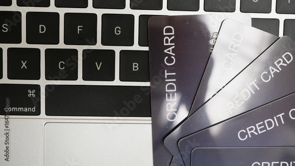 Fototapeta Close up image of laptop keyboard with several credit cards fanned out on top, suggesting online shopping or digital transactions