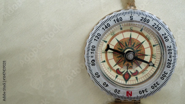 Fototapeta Vintage compass with detailed rose design is shown against textured beige background, highlighting its intricate markings and directional indicators