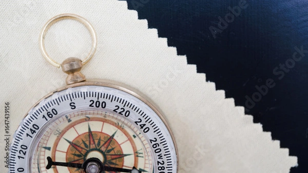 Fototapeta Vintage compass with brass ring rests on textured surface, partially covered by piece of fabric. compass needle points north, evoking sense of adventure and exploration