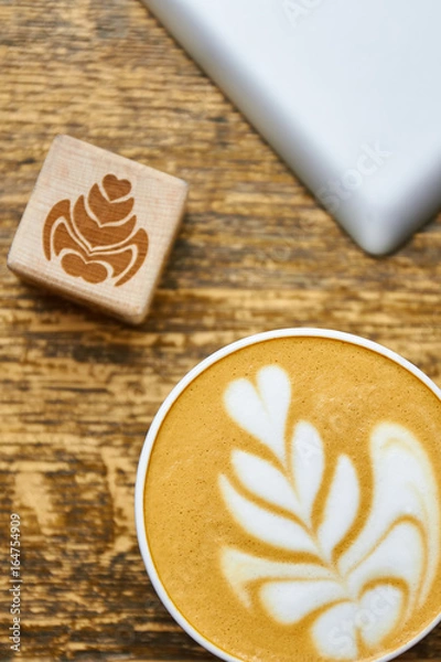 Fototapeta Coffee foam top view. Wooden cube with flower picture. Latte art basics.