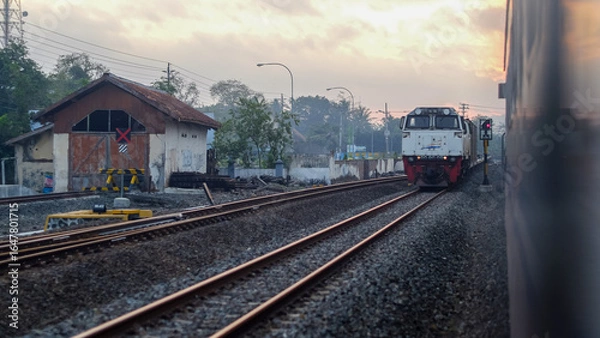 Fototapeta Indonesian Train Passing Through Railway Tracks at Sunset in a Small Town