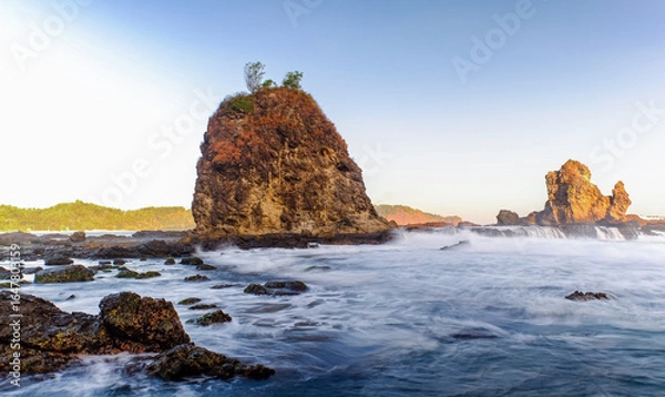 Fototapeta Dramatic Seaside Landscape with Long Exposure, Smooth Wave, Rocks and Sunset in Yogyakarta, Indonesia