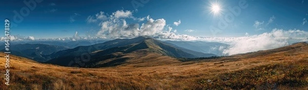 Fototapeta Panoramic view of mountain peaks and valleys under a vibrant sky.  Golden-toned meadows stretch across the foreground, leading to rugged, 