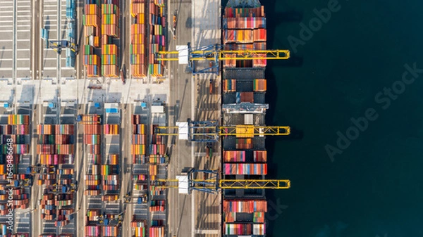 Obraz Top view of a large cargo ship loading and unloading containers at a deep-sea port. This aerial scene highlights global logistics, international trade, and maritime transportation hubs.