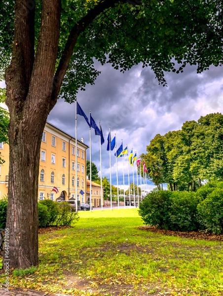 Obraz Public park near president palace with waiving flags of Latvia, European Union and Ukraine near façade of governmental buildings, historic  center of old Riga city - the capital of Latvia 