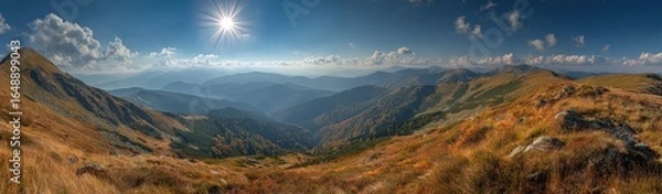 Fototapeta Panoramic mountain vista.  Autumnal peaks and valleys stretch into the distance under a bright sun.  A golden-brown landscape of high, rolling hills, dotted with hardy vegetation, leads to a hazy.