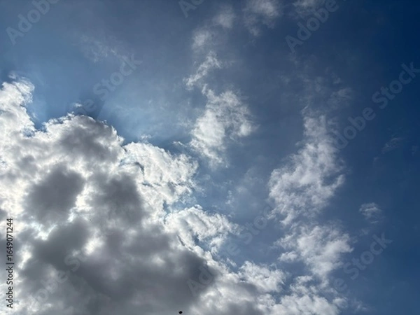 Fototapeta Bright blue sky with a smooth spread of white clouds, sunlight is seen spreading softly from behind the cloud layer in the middle, creating a calm and peaceful atmosphere.