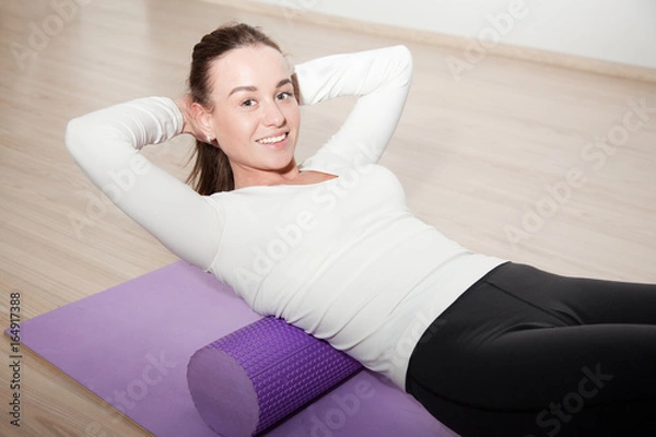 Fototapeta attractive girl coach demonstrates exercises myofascial relaxation on the foam roller