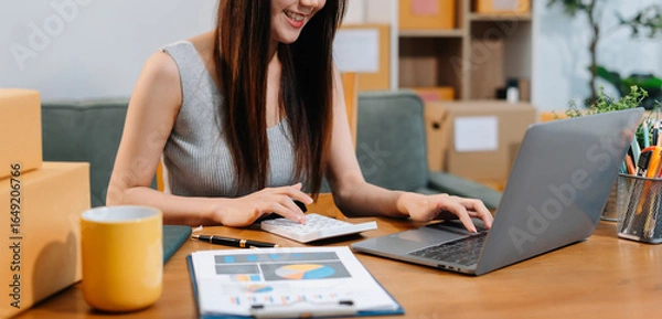 Fototapeta Business owner using calculator and smart phone working at home office.