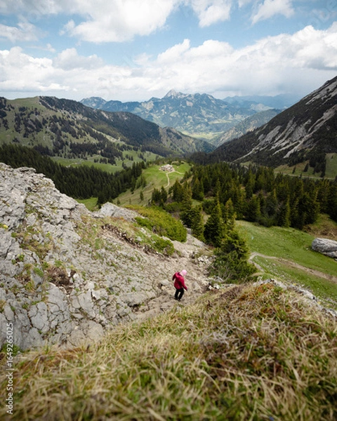 Fototapeta Hiker in Red Jacket Descending Rocky Mountain Slope with Scenic Valley View