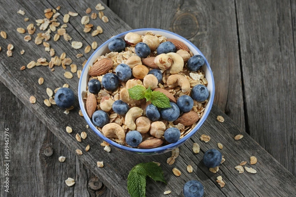 Obraz Granola with nuts and fresh blueberries in glass bowl over old wood background.