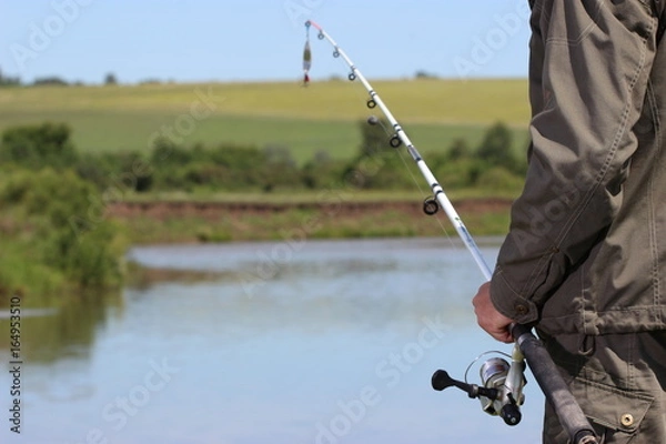 Fototapeta Рыболов со спиннингом в руке ловит рыбу на берегу озера