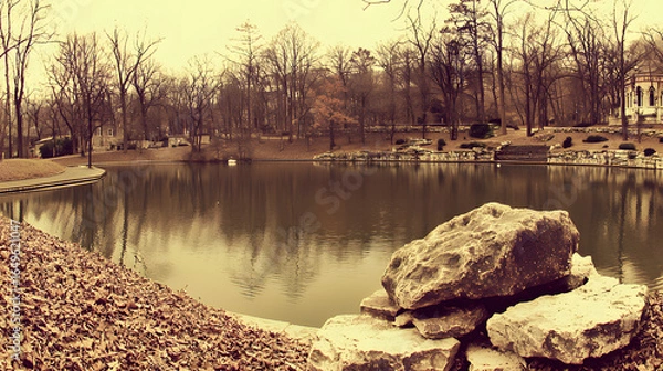 Fototapeta Tranquil pond featuring a large rock in the center surrounded by lush greenery and water
