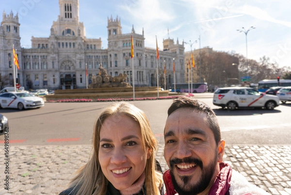 Fototapeta City Exploration: A couple smiling gleefully pose in front of a stunning architectural marvel. A dynamic portrayal of exploration and tourism.