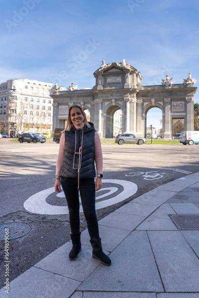 Fototapeta Urban Explorer by the Arch: A traveler finds joy in her journey, she poses in front of a historical landmark with an architectural marvel standing tall against the backdrop of a bustling city.