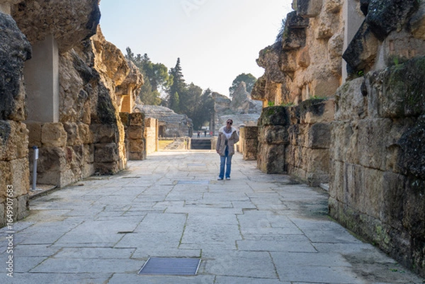 Fototapeta Explorer of the Ancient Ruins of Italica: A lone explorer examines an ancient Roman structure, bathed in golden light, evoking a sense of history and wanderlust.