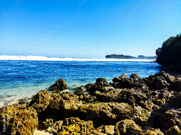 Fototapeta A tranquil beach with crystal clear water and a vibrant coral reef. Tranquil beach scene with clear turquoise water, light sandy shore, and dark coral rocks. Bright sunny day. 