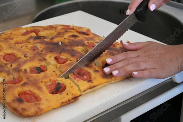 Obraz mani tagliano una focaccia fatta in casa con un grande coltello