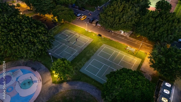 Fototapeta Aerial View of Illuminated tennis courts at Dusk Surrounded by Lush Green Trees