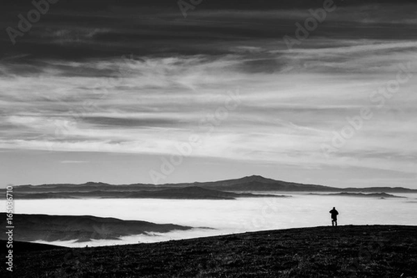 Fototapeta A man in a mountains scenery, with fog filling a valley and a big, deep sky