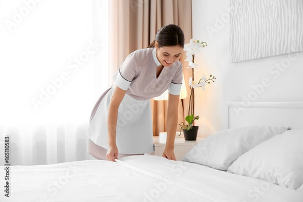 Obraz Młoda pokojówka ścielenie łóżka w jasnym pokoju hotelowym