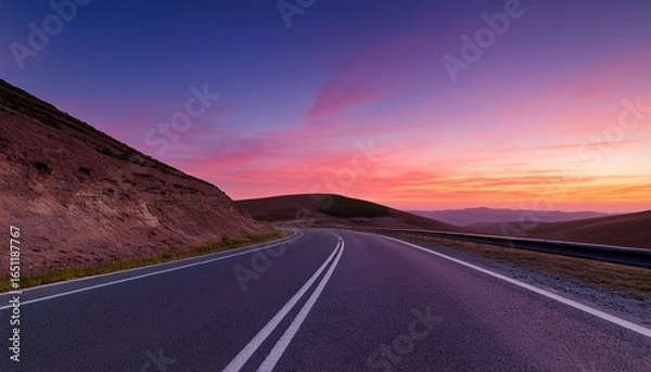 Fototapeta an empty road at twilight with the sky filled with warm hues of pink and purple the paved highway stretches into the distance curving around hills under a clear sky