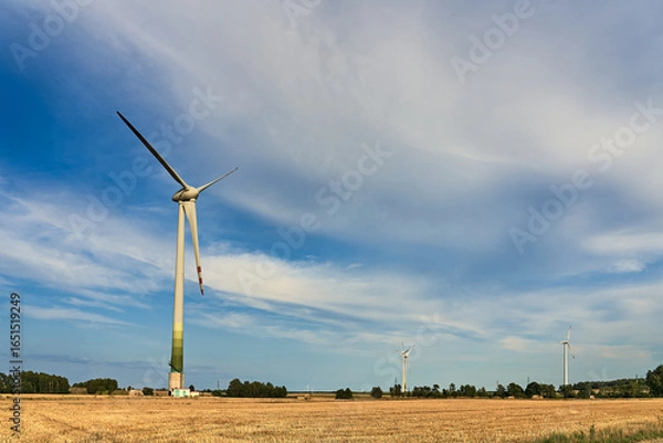 Fototapeta A wind turbine in a golden harvested field under a dramatic cloudy sky