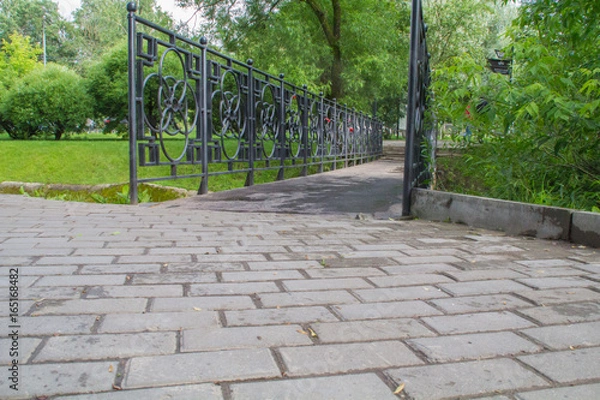 Obraz Forged bridge railing through a small river in the park. Locks on the railing, as a symbol of eternal love for the newlyweds.