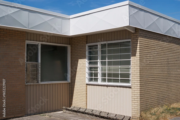 Obraz A beige brick wall with a barred window and concrete ground under sunlight in Hope, British Columbia, Canada.
