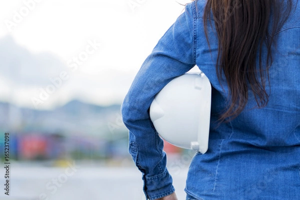 Fototapeta Professional Woman Engineer Holding White Helmet, Standing at Construction site for measure the construction worker - Engineering Concept