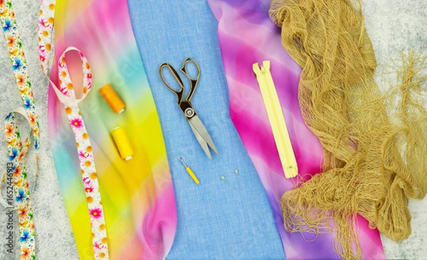 Fototapeta Panorama of fabrics and sewing accessories. Silk colorful fabric, tailor's scissors, spools of thread, zipper and tape for sewing clothes.