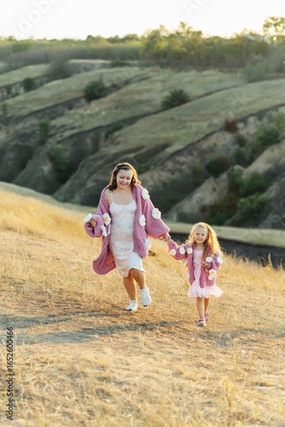 Fototapeta A young mother and daughter are walking in nature among the mountains in beautiful identical sweaters