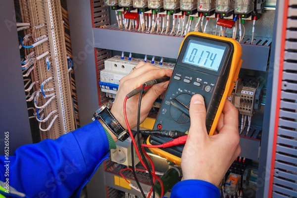 Fototapeta Inżynier elektryk dostosowuje sprzęt elektryczny z multimetrem w jego dłoni zbliżenie.