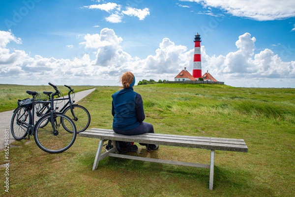 Fototapeta Touristin auf einer Bank und Fahrräder vor dem Leuchtturm Westerheversand