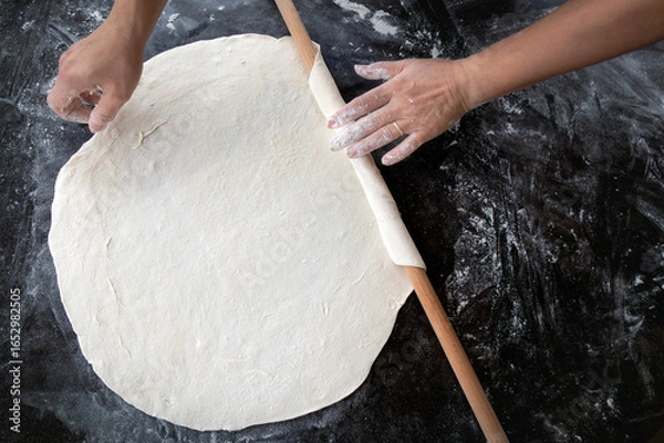 Fototapeta Hands rolling dough on a wooden table — traditional homemade cooking process