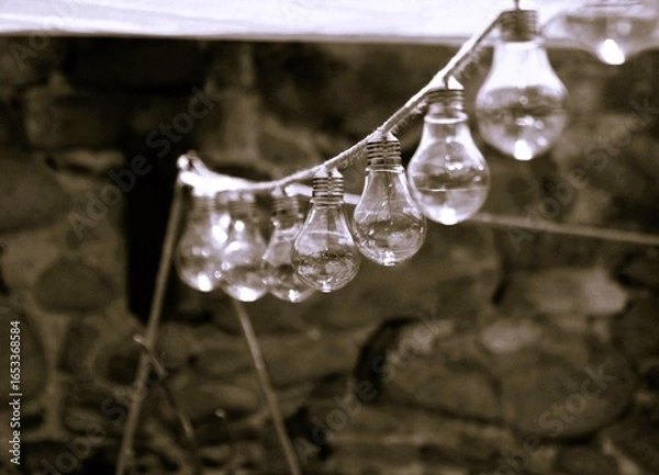 Obraz Lampadine appese in fila, sfondo di pietre, luce soffusa.
