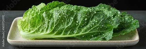 Obraz Fresh, vibrant green cabbage leaves on a light beige rectangular plate, covered in water droplets
