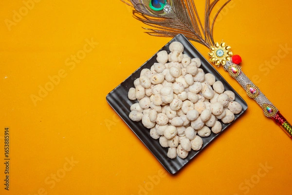 Fototapeta Traditional Prasad Makhana Offering with Decorative Peacock Feather on Yellow Background