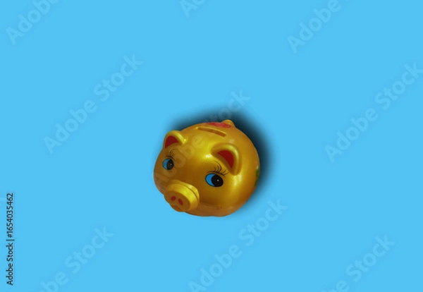 Fototapeta Closeup piggy bank gold color isolated on blue background for stock photo. saving concept, finance, investment, cyan floor