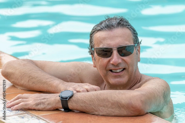 Fototapeta A handsome wet man is leaning with his arms on the edge of the pool, with his body in the water